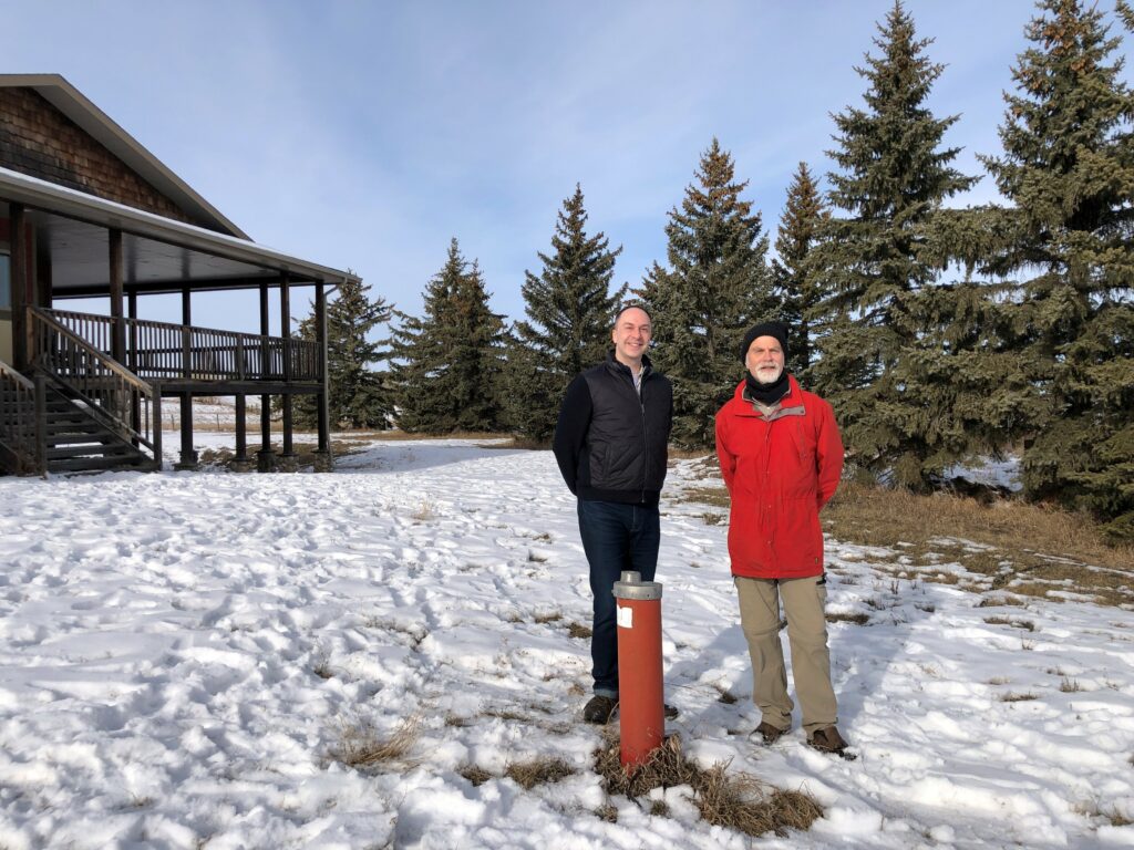 Dr. Aaron Goodarzi (Left) and Henk de Haan (Right) stand beside a water well on de Haan’s property near Okotoks, AB. (Photo Credit: Joshua Rice, Arnie Charbonneau Cancer Institute)