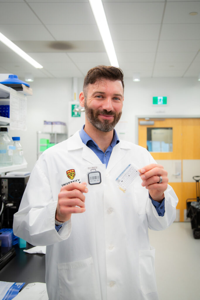 Dr. Dustin Pearson holding a radon test kit and a toenail sample collection bag (Credit: Glynnis Mutch Photography)